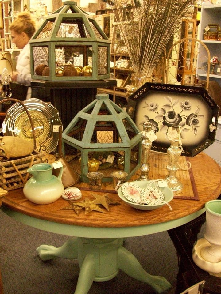 Mint-green painted pedestal table topped with glass cloches, vintage ceramics, and collectibles