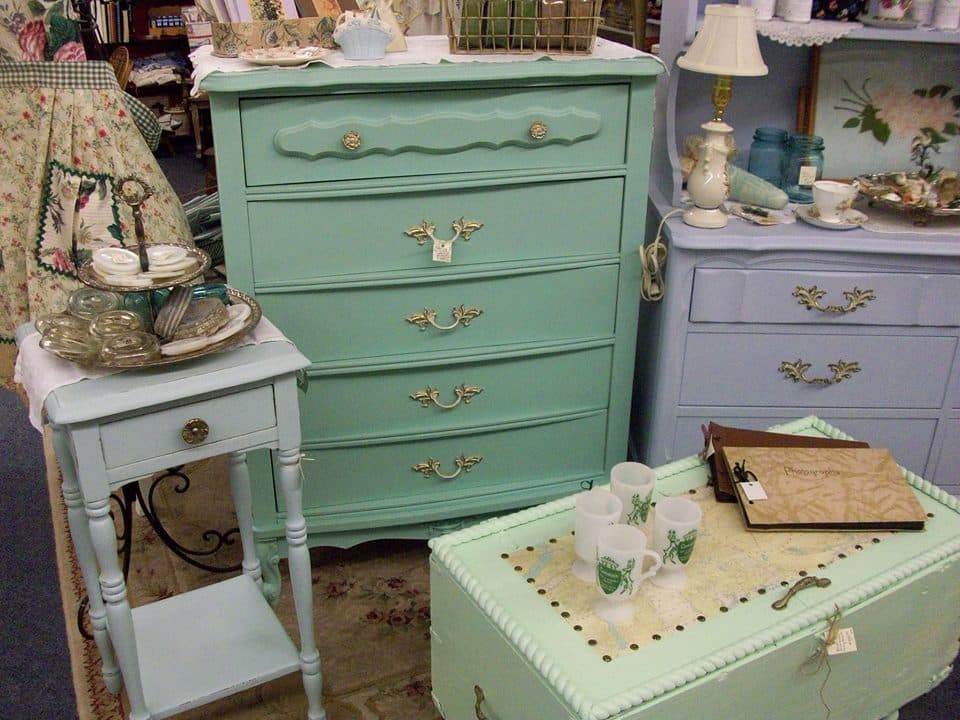 Chalk-painted furniture grouping: a teal chest of drawers, a lavender dresser, and a white side table with a teacup set