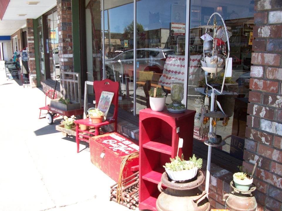 Storefront on a sunny day with red painted furniture and potted succulents displayed on the sidewalk